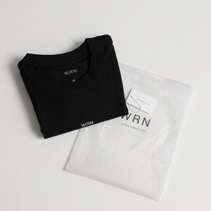 May include: A black t-shirt with the brand name "WRN" printed in white, folded neatly next to a white plastic bag. The bag contains a tag with the brand name and the words "Structured Form".