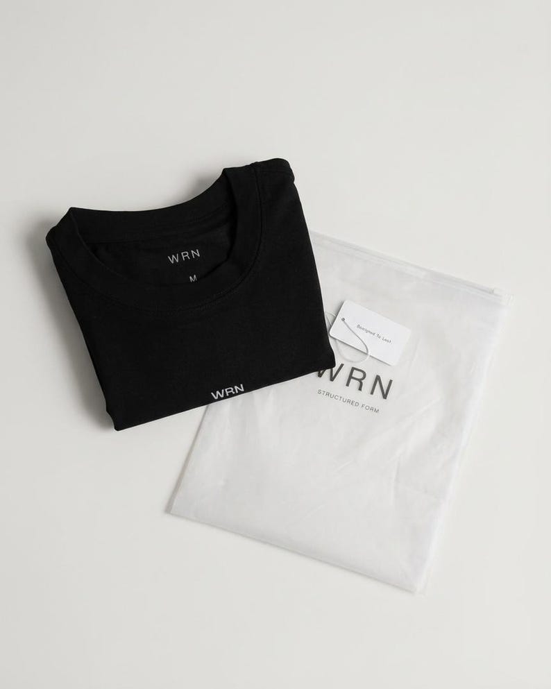 May include: A black t-shirt with the brand name "WRN" printed in white, folded neatly next to a white plastic bag. The bag contains a tag with the brand name and the words "Structured Form".