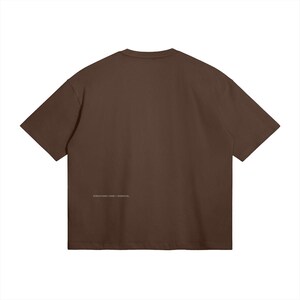May include: A solid brown t-shirt with short sleeves. The back of the shirt features the text "STRUCTURE FORM / ESSENTIAL" in small, light-colored lettering near the bottom hem. The shirt is made of a soft, opaque material.