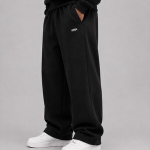 Puede incluir: Pantalones de ch&aacute;ndal negros con silueta de pierna ancha y cintura el&aacute;stica. El texto WRN est&aacute; impreso en blanco en la parte superior del muslo izquierdo. Estos pantalones se combinan con zapatillas blancas, creando un estilo casual y s&oacute;lido.