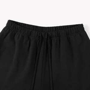 May include: Close-up of black sweatpants with an elasticated waistband and drawstring. The trousers are made of a soft, dark fabric. The image highlights the details of the waistband and the drawstring closure.
