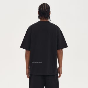 May include: Black oversized t-shirt with short sleeves. The back of the shirt features the text "STRUCTURED FORM / ESSENTIAL" in a small, white font. The model is wearing black shorts.