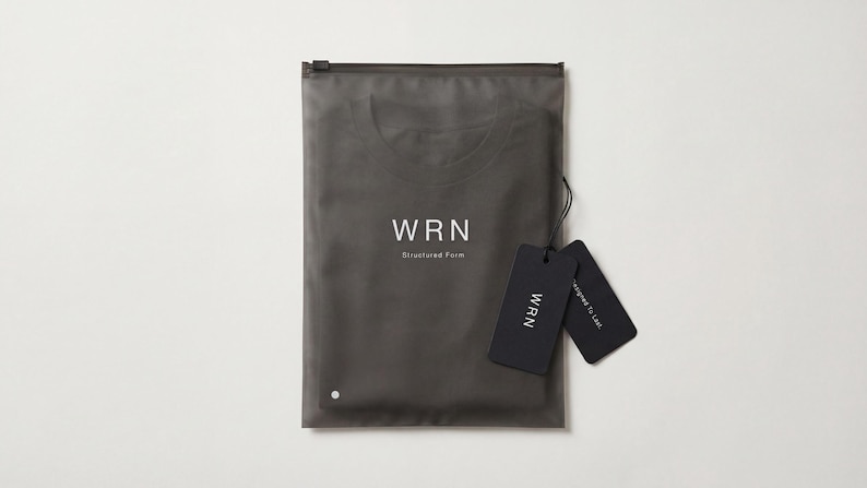 May include: A dark gray garment is packaged in a matching zip-up bag. The bag has the white text "WRN Structured Form". Two black tags with the "WRN" logo and other text are attached.