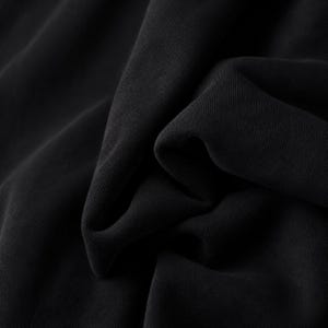 K&ouml;nnte beinhalten: Ein einfarbiger schwarzer Stoff mit glatter, matter Textur, der tiefe, weiche Falten und kaskadierende Drapierungen aufweist, die eine Reihe von Schatten und Lichtern auf der Oberfl&auml;che erzeugen und die dichte, gleichm&auml;&szlig;ige Farbe betonen.