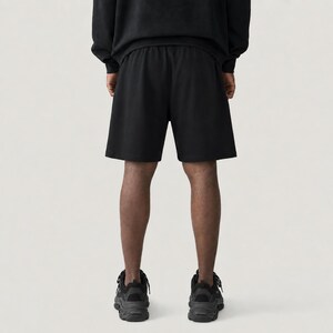May include: Black athletic shorts with an elasticated waistband. The shorts are part of a matching set, paired with a black sweatshirt. The person is wearing black athletic shoes. The image is taken from a rear view.