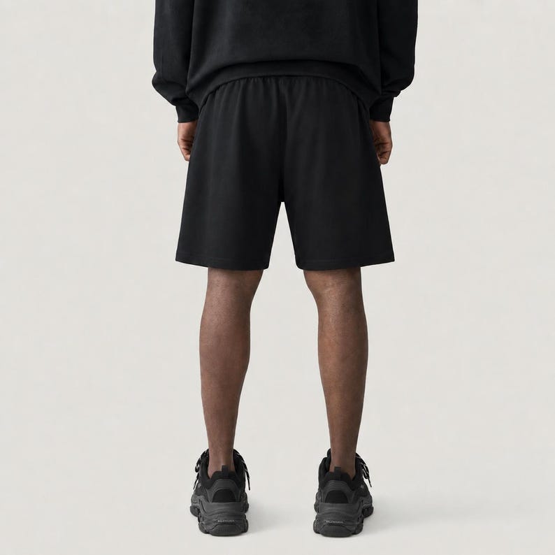 May include: Black athletic shorts with an elasticated waistband. The shorts are part of a matching set, paired with a black sweatshirt. The person is wearing black athletic shoes. The image is taken from a rear view.