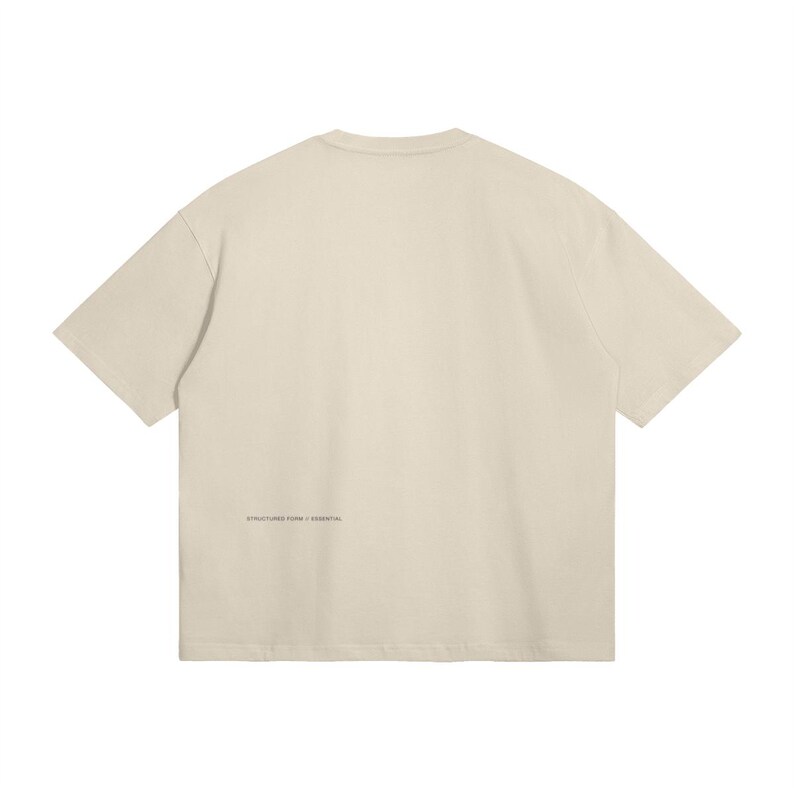 May include: Cream-colored, oversized t-shirt. The back of the shirt features the text "STRUCTURED FORM / ESSENTIAL" printed in a small, dark font near the bottom hem. The shirt has short sleeves and a crew neck.