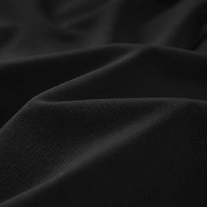May include: Close-up of black fabric with a textured surface. The fabric is draped, creating soft folds and shadows. The material appears to be a medium-weight textile, suitable for clothing or home decor.
