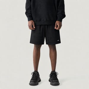 May include: Black shorts with a drawstring waist and a small white logo. The shorts are paired with a black hoodie and black trainers with patterned laces. The outfit is casual and sporty.