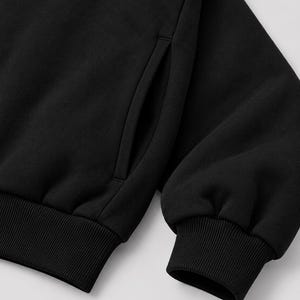 K&ouml;nnte beinhalten: Ein einfarbiges schwarzes Sweatshirt mit einem langen &Auml;rmel, einem gerippten B&uuml;ndchen und einer vertikalen Seitentaschen&ouml;ffnung. Das Kleidungsst&uuml;ck besteht aus einem weichen, fleeceartigen Stoff mit einer durchgehend mattschwarzen Oberfl&auml;che.