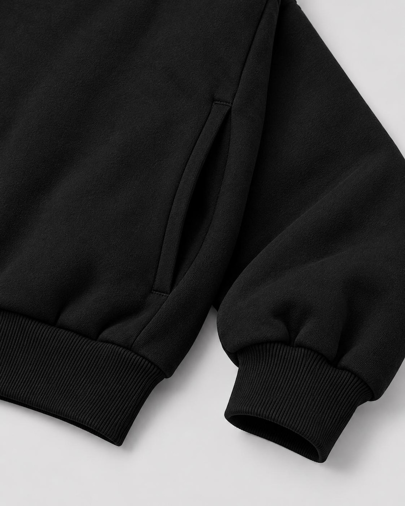 K&ouml;nnte beinhalten: Ein einfarbiges schwarzes Sweatshirt mit einem langen &Auml;rmel, einem gerippten B&uuml;ndchen und einer vertikalen Seitentaschen&ouml;ffnung. Das Kleidungsst&uuml;ck besteht aus einem weichen, fleeceartigen Stoff mit einer durchgehend mattschwarzen Oberfl&auml;che.