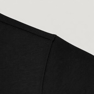 May include: Close-up of a black t-shirt shoulder and neckline. The fabric has a subtle texture, and the seams are neatly stitched. The shirt appears to be made of a soft, comfortable material.