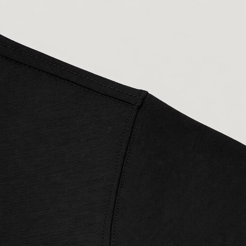 May include: Close-up of a black t-shirt shoulder and neckline. The fabric has a subtle texture, and the seams are neatly stitched. The shirt appears to be made of a soft, comfortable material.