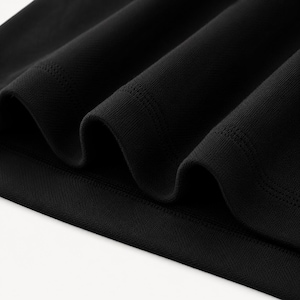 May include: Close-up of black fabric with a textured, ribbed appearance. The material is folded, creating deep shadows and highlighting the fabric's weave. The edges of the fabric are smooth and finished.