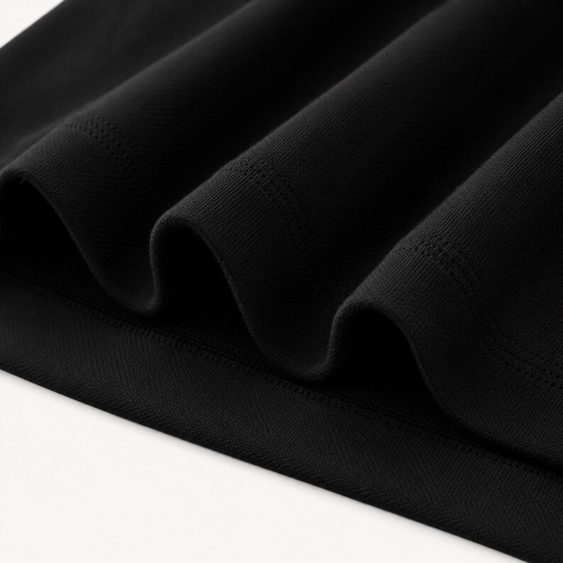 May include: Close-up of black fabric with a textured, ribbed appearance. The material is folded, creating deep shadows and highlighting the fabric's weave. The edges of the fabric are smooth and finished.