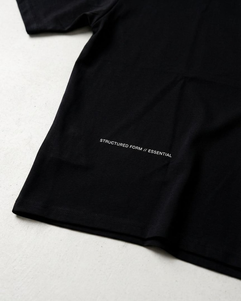 May include: A black t-shirt with the text "STRUCTURED FORM // ESSENTIAL" printed in white near the bottom. The shirt is made of a soft material and has a simple, minimalist design.