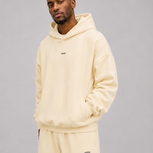 May include: A cream-coloured hooded sweatshirt featuring a front kangaroo pocket and the letters WRN printed in small black font on the centre of the chest. The matching cream-coloured sweatpants also feature the letters WRN in black on the leg.