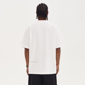 May include: A white, short-sleeved t-shirt with the text "STRUCTURED FORM + ESSENTIAL" printed in black near the hem. The shirt is paired with black shorts. The model is facing away from the camera.