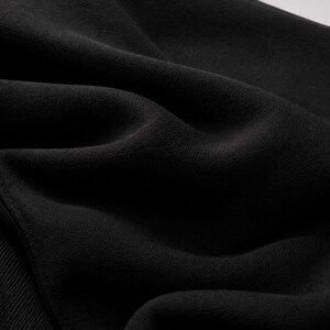 Puede incluir: Una tela negra s&oacute;lida con una textura suave y mate, con pliegues visibles que crean sombras y reflejos profundos en la superficie. El material presenta un sutil detalle de punto acanalado en el borde inferior izquierdo, de tono oscuro.
