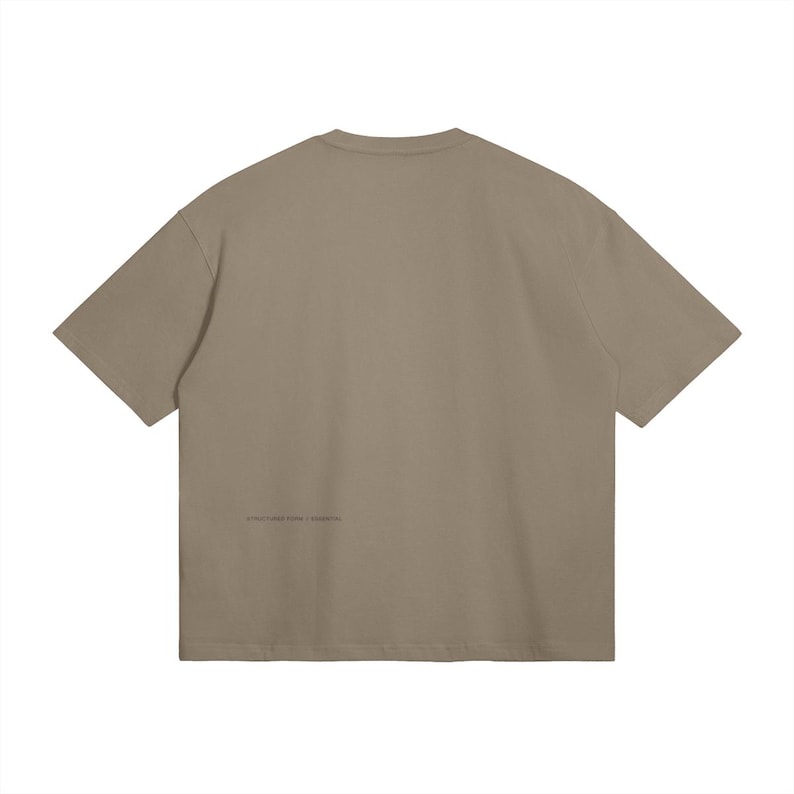 May include: A taupe-colored, short-sleeved t-shirt. The back of the shirt features a small, printed text near the bottom. The shirt has a relaxed fit and a crew neck.