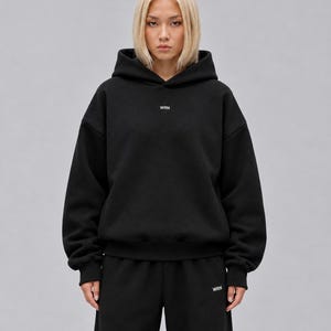 A black long-sleeve hooded sweatshirt featuring a hood, ribbed cuffs, and a ribbed hem. The text WRN is printed in small white capital letters on the centre of the chest. The garment has a relaxed fit with dropped shoulders.