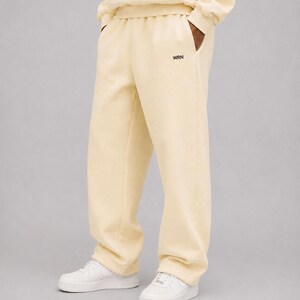 K&ouml;nnte beinhalten: Hellgelbe Jogginghose mit lockerer Passform, elastischem Bund und den Buchstaben WRN in kleiner schwarzer Schrift nahe der linken Tasche. Die Hose wird mit wei&szlig;en Sneakern und einem passenden hellgelben Sweatshirt kombiniert.
