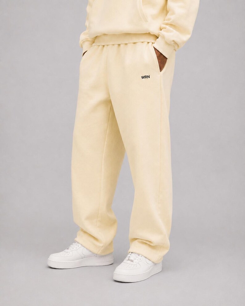 K&ouml;nnte beinhalten: Hellgelbe Jogginghose mit lockerer Passform, elastischem Bund und den Buchstaben WRN in kleiner schwarzer Schrift nahe der linken Tasche. Die Hose wird mit wei&szlig;en Sneakern und einem passenden hellgelben Sweatshirt kombiniert.