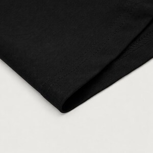 May include: Close-up of a section of black fabric, possibly a garment. The fabric has a smooth texture and is folded over, revealing a seam with visible stitching. The image is well-lit, highlighting the details of the material.