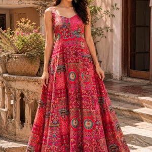 May include: A sleeveless, floor-length red dress with a vibrant, intricate pattern. The dress features a V-neckline and a full skirt, showcasing a mix of floral and geometric designs. The overall style is elegant and suitable for special occasions.