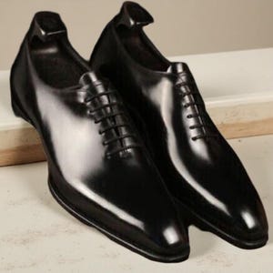May include: A pair of shiny black leather dress shoes with a traditional lace-up design. The shoes have a polished finish, and are shown with shoe trees inside to keep their shape. The shoes are a formal style.