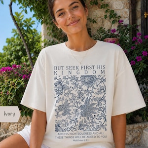 Könnte beinhalten: Ein elfenbeinfarbenes T-Shirt mit kurzen Ärmeln, einem blauen Blumenmuster und dem Text BUT SEEK FIRST HIS KINGDOM AND HIS RIGHTEOUSNESS AND ALL THESE THINGS WILL BE ADDED TO YOU Matthew 6:33 in dunkelblauer Schrift auf der Vorderseite.