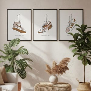 Peut inclure: Trois impressions encadrées présentant des dessins au trait de baskets. La première impression montre une Air Jordan 1 montante, la seconde une Air Max 90 et la troisième une Adidas Superstar. Chaque impression a une palette de couleurs neutres avec des tons bruns et beiges.
