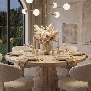 Round breakfast table with travertine finish styled with plates, cups and modern dining chairs in a bright kitchen space