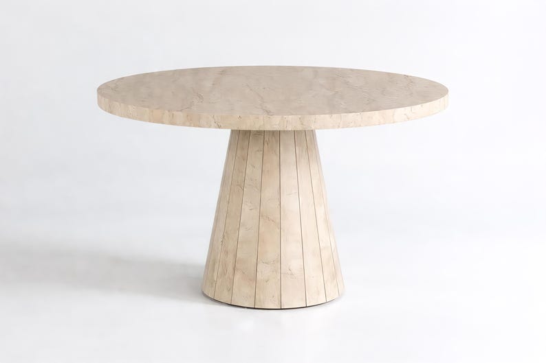 Round pedestal dining table in warm neutral interior with decorative vase and elegant table setting