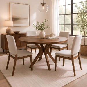 May include: A round wooden dining table with a dark brown finish and a central pedestal base, surrounded by four chairs featuring light beige upholstered seats and backrests with matching wooden legs, arranged on a light-coloured area rug.