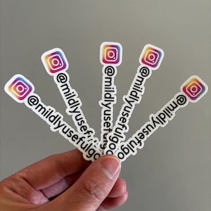 May include: A hand holding five white stickers with the Instagram logo and the text "@mildlyusefulgo". The Instagram logo is a square with a gradient of orange, pink, and purple.