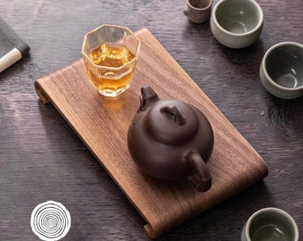 May include: A wooden tea tray with a brown teapot, a faceted glass of tea, and several small ceramic cups. The tray has curved edges. The logo "CARVEDWORKS EST. 2025" is in the lower left corner.