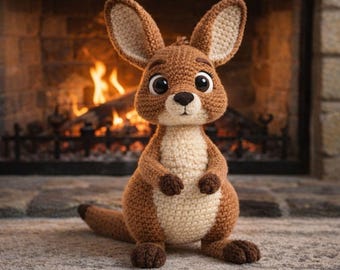 May include: A handmade crochet kangaroo toy in shades of brown and cream, with large, expressive eyes. The kangaroo is sitting on a stone surface, with a fireplace and flames in the background. The toy has a long tail and small arms.