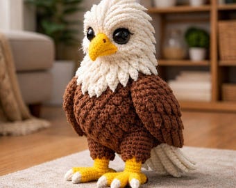 May include: A handcrafted crochet eagle figurine. The eagle features a white head and tail, a brown body and wings, and yellow feet with white claws. The eagle has large black eyes and a yellow beak. The figurine is standing on a neutral-colored rug.
