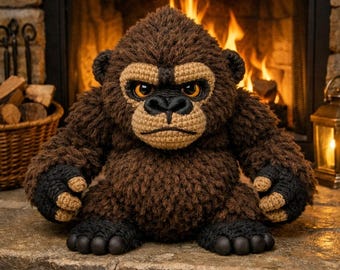 May include: A handmade, brown crochet gorilla with black hands and feet, and orange eyes. The plush toy is sitting on a stone hearth in front of a fireplace. A cozy, decorative item.