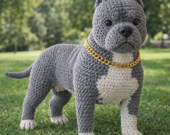 May include: A crocheted dog sculpture in shades of gray and white, with a gold-colored chain collar. The dog is standing on green grass, with a blurred background of trees. The handmade dog has a realistic appearance.