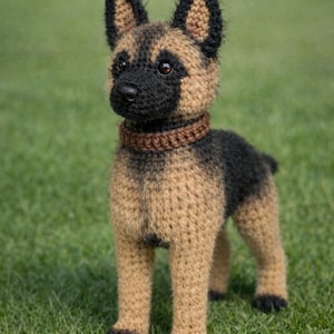 Puede incluir: Figura de perro Pastor Alemán de ganchillo. El perro es marrón y negro, con un collar marrón. El perro está de pie sobre hierba verde.