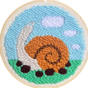Op de afbeelding: Een afgewerkte punch needle borduurring met een slakkenontwerp. De slak heeft een oranje huisje en een grijze body, tegen een blauwe lucht met witte wolken en groen gras. Het kunstwerk is ingelijst in een houten ring.