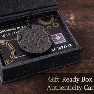 May include: A dark grey pendant with a circular design, presented in a black gift box with an authenticity card. The pendant has a central circular pattern surrounded by smaller circles. The box is labelled with text including "Gift-Ready Box + Authenticity Card".