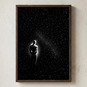以下が含まれることがあります： 星空を背景に、スポットライトの下に立つシルエットの人物を描いた白黒のアートプリント。アートワークは濃い木製のフレームに収められており、印象的なコントラストを生み出しています。