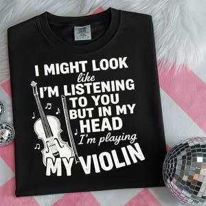 Könnte beinhalten: Schwarzes Sweatshirt mit weißem Text und einer Geigen-Grafik. Der Text lautet: "I MIGHT LOOK like I'M LISTENING TO YOU BUT IN MY HEAD I'm playing MY VIOLIN". Das Sweatshirt hat einen Rundhalsausschnitt und lange Ärmel.