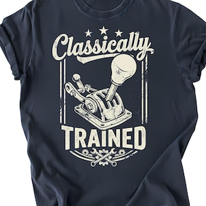 Może przedstawiać: Granatowa koszulka z postarzaną grafiką dźwigni zmiany biegów i napisem "Classically Trained" w stylu vintage. Projekt zawiera gwiazdy, klucze i koła zębate, tworząc motyw klasycznych samochodów.