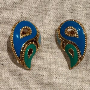 May include: A pair of teardrop-shaped earrings featuring gold-tone metal edges with a beaded texture. Each earring contains two distinct sections of enamel inlay in bright blue and vibrant green, surrounding open cut-out centers.