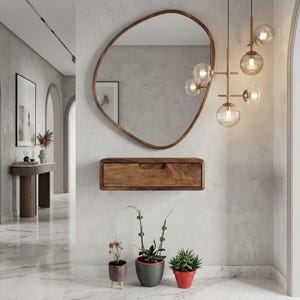 Puede incluir: Un espejo de pared de forma org&aacute;nica irregular con un marco de madera fino, una consola de caj&oacute;n rectangular flotante de madera y una l&aacute;mpara colgante de lat&oacute;n de varios brazos con cinco pantallas de cristal estriado.