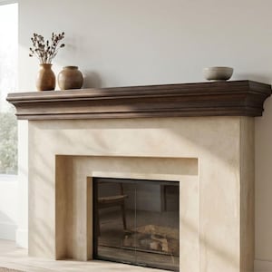 Può includere: Un camino con un caminetto in legno marrone scuro e una cornice in pietra colorata. Il caminetto contiene due vasi marroni con piante essiccate e una piccola ciotola grigia. Il camino ha una porta a vetri.